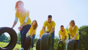 Fun Outdoor Team Activities in London Alt: A group in yellow shirts rolling tires outdoors, enjoying a team-building activity in a sunny, grassy area.