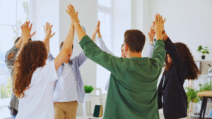 Team celebration with six people raising hands in a circle in a bright office, fostering unity and morale.